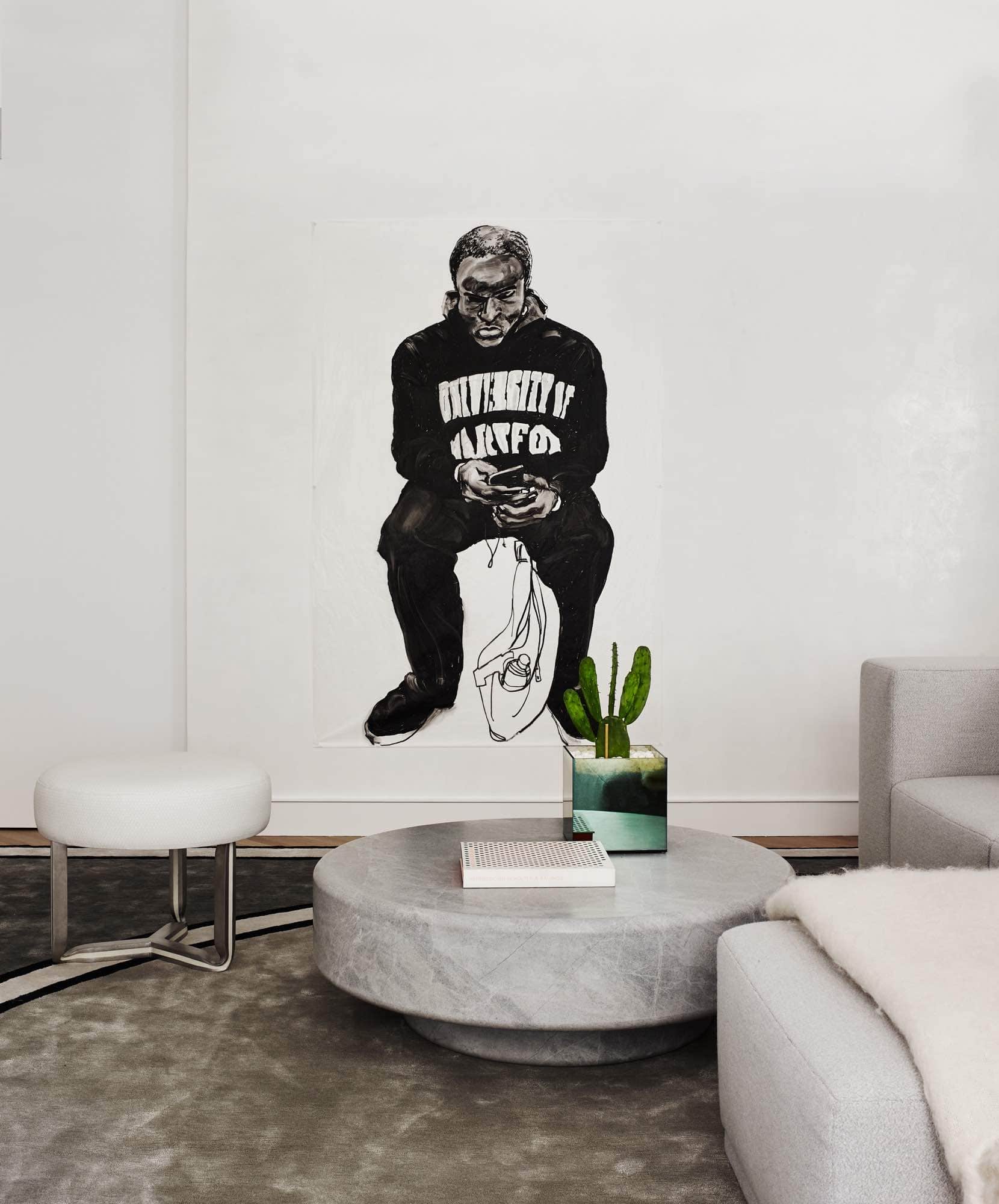 Designed by Carol Egan, this image shows a detail of the living room of a Park Avenue apartment with an oil on glassine paper overscale portrait drawing by Jack Ceglic.  Also in the frame is a Blue de Savoy stone coffee table next to a custom modular sofa upholstered in a grey boucle fabric.  A stainless steel and resin ottoman designed by Studio Carol Egan is upholstered in a stamped hexagonal shaped white leather.