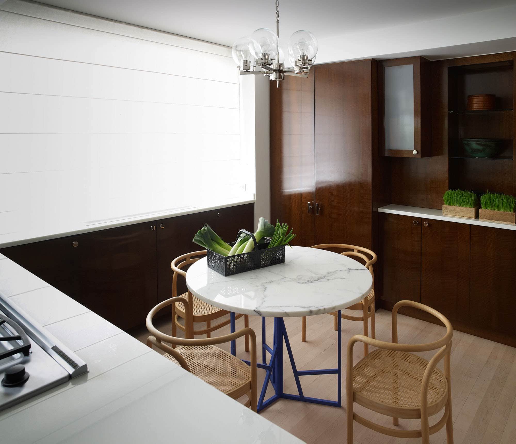 This image shows a powder room with a white Corian framework enclosing the sink and niche shelves below the sink.  The room is painted in a pantone modern green color contrasting the white Corian framed sink wall.  Hung on the Corian wall is a modernist mirror with steel frame and vintage train travel cases by Louis Vuitton.