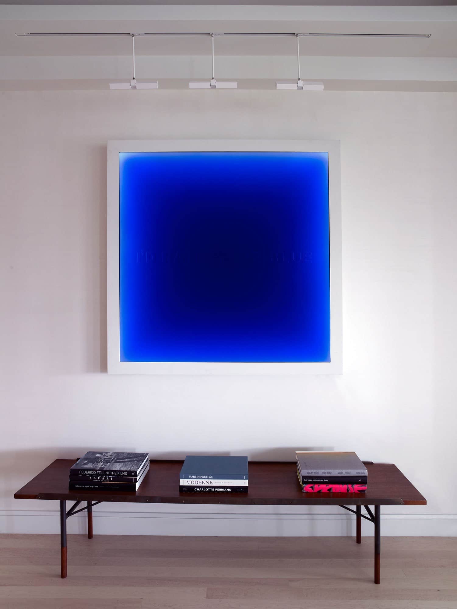 Shown in this image, is an ‘I’d Rather Be Blue’ artwork by Matilde Alessandra above a bench by House of Finn Juhl.  The artwork is hung in the hallway of the Avenue apartment designed by Carol Egan.