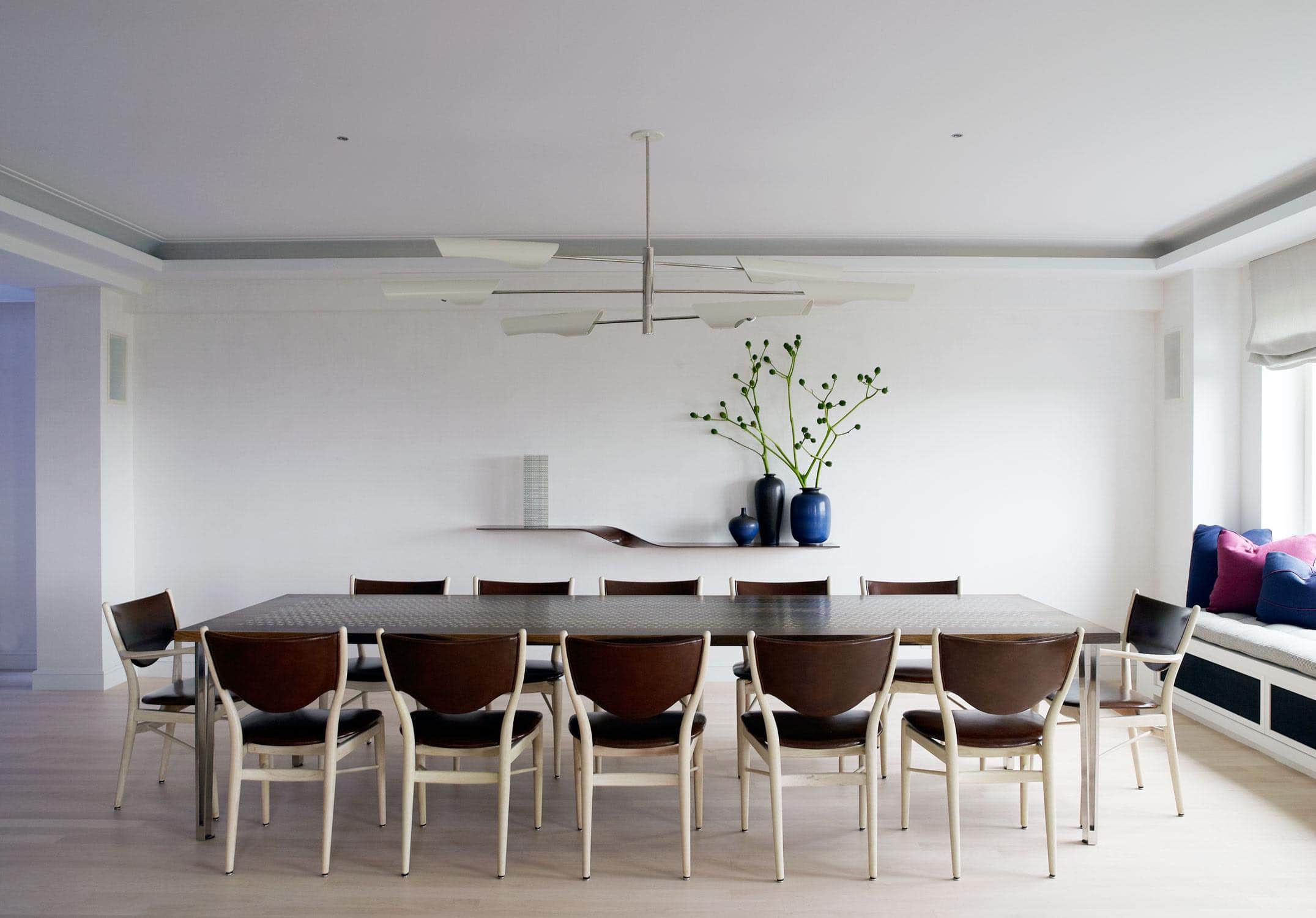 In this dining room designed by Carol Egan, the smoked Oak and bronze inlaid Baer dining table from Khouri Guzman Bunce is surrounded by dining chairs by Hans J. Wegner.  This room is lit by a three tiered ""Torroja Cross"" chandelier by David Weeks.