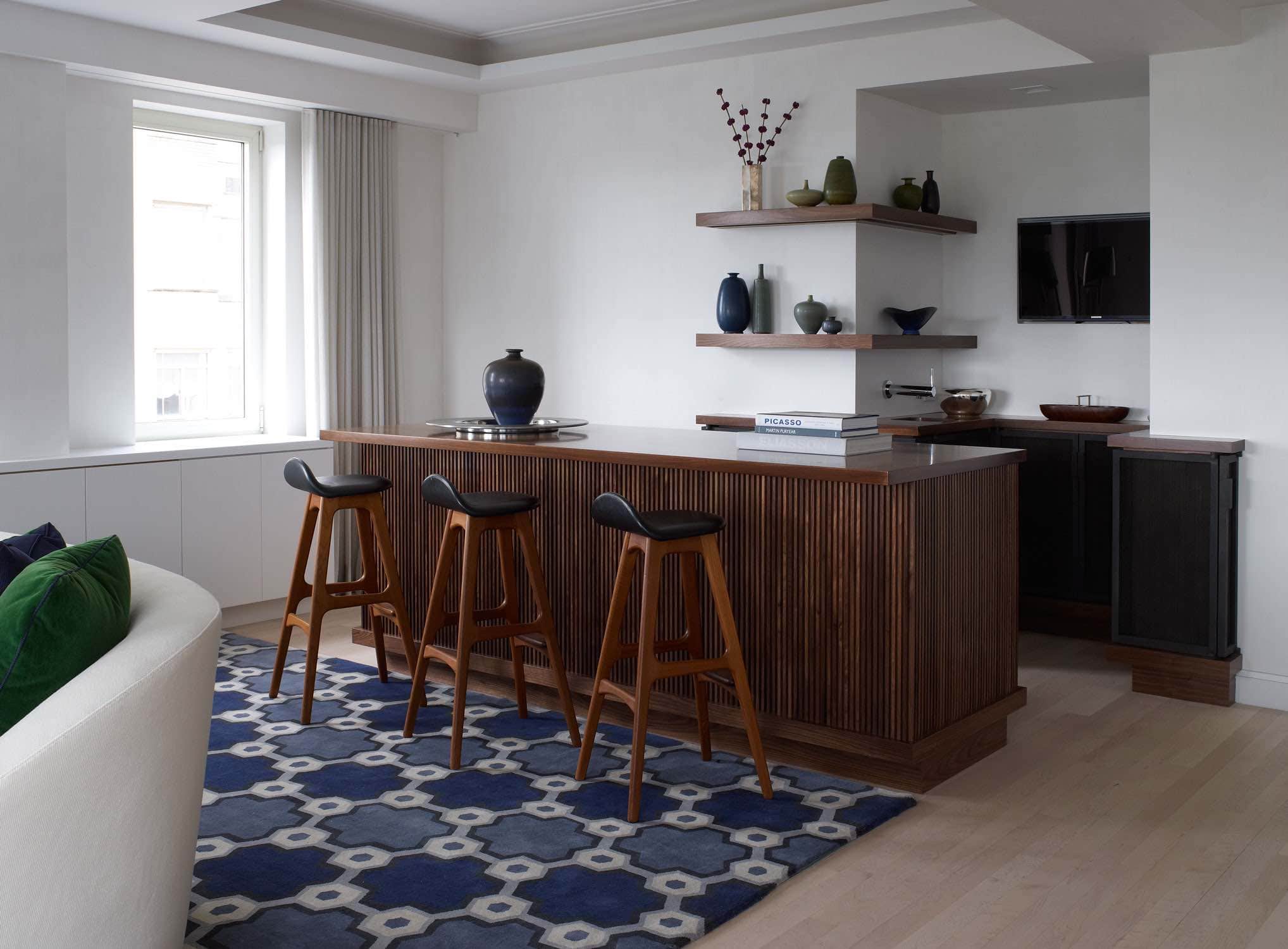 Shown in this image is the view of the bar area in the living room of a Fifth avenue apartment in walnut designed by Carol Egan with vintage danish wood and leather Erik Buck bar stools.  The bar is custom made with bronze mesh doors and walnut slatted millwork.