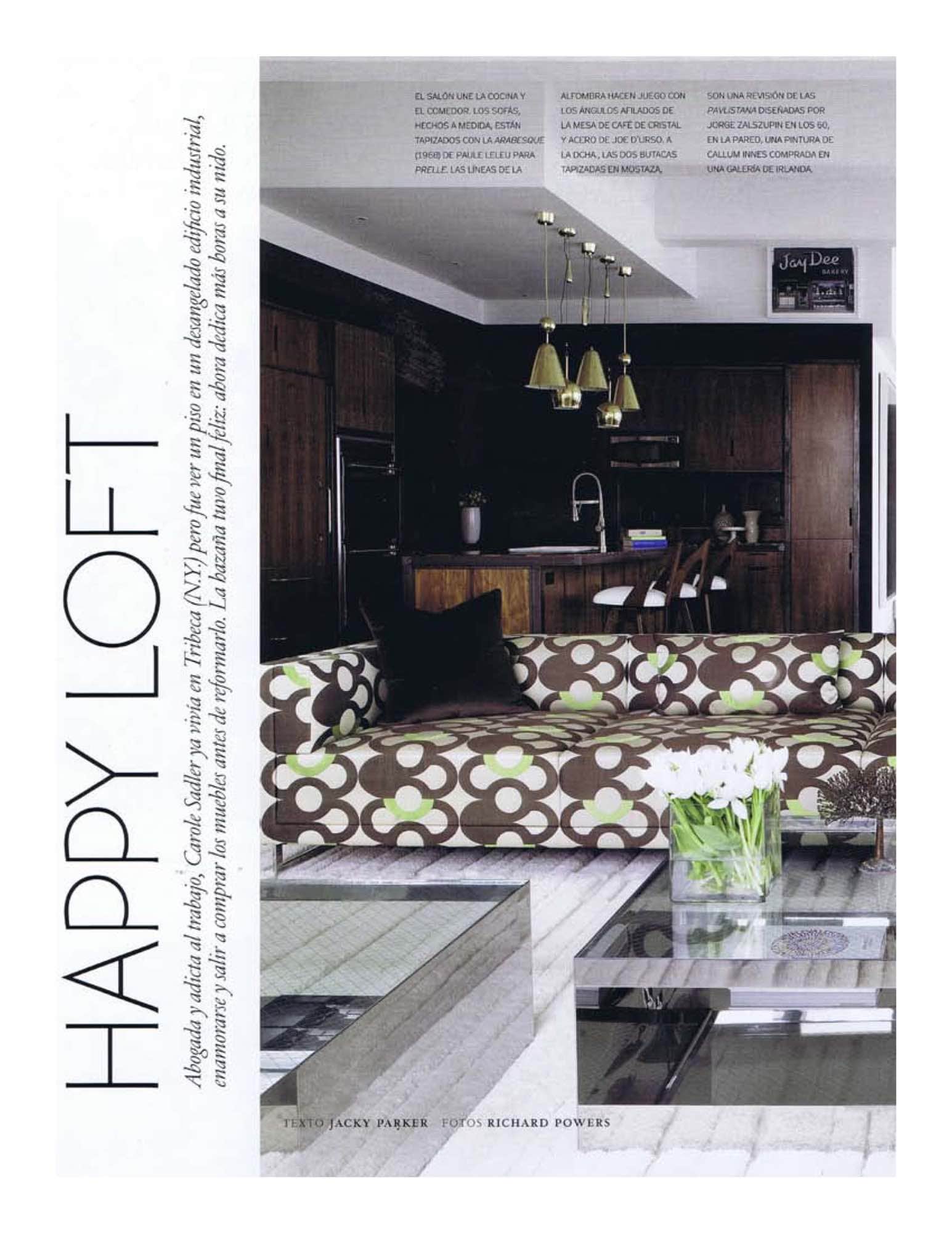 Photograph of a living room with custom sofa design by Studio Carol Egan in Prelle fabric by Leleu, glass and steel coffee table by Joe D Urso.  Walnut kitchen units are offset by 50s brass Paavo Tynell pendant lights.  Inteiror design by Carol Egan.