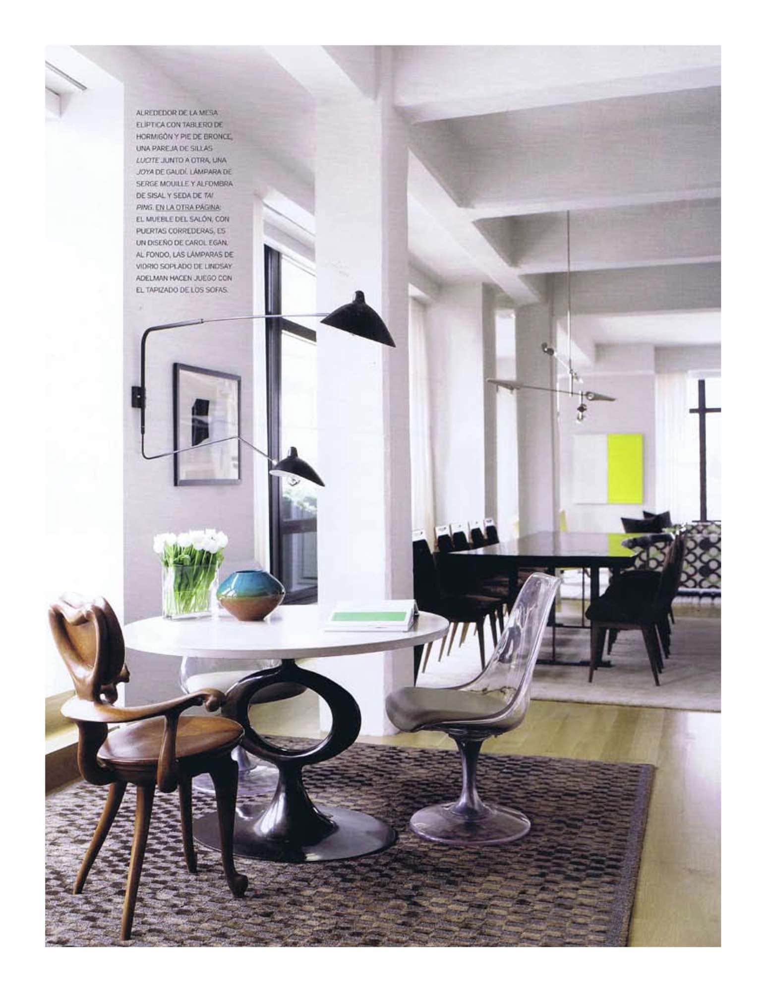A photograph of breakfast area, designed by Carol Egan Interiors, with an elliptical table which has a poured concrete top and bronze base.  A pair of shapely Lucite chairs and an unusual Gaudi chair are complementary.  Tai Ping sisal and silk rug.